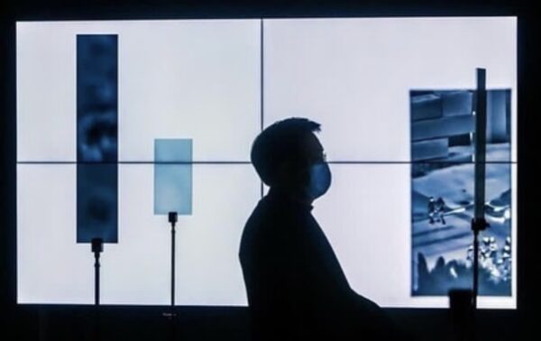 silhouette of a person in front of white tv screens with smaller screens in front revealing parts of an image on the white screens