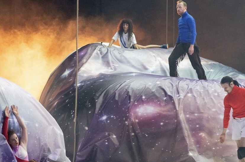 people standing leaning and laying on a large object on a stage draped in a space scene printed fabric