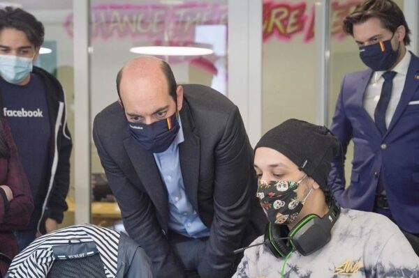 three people in face masks look over the shoulder of a fourth person sitting at a computer