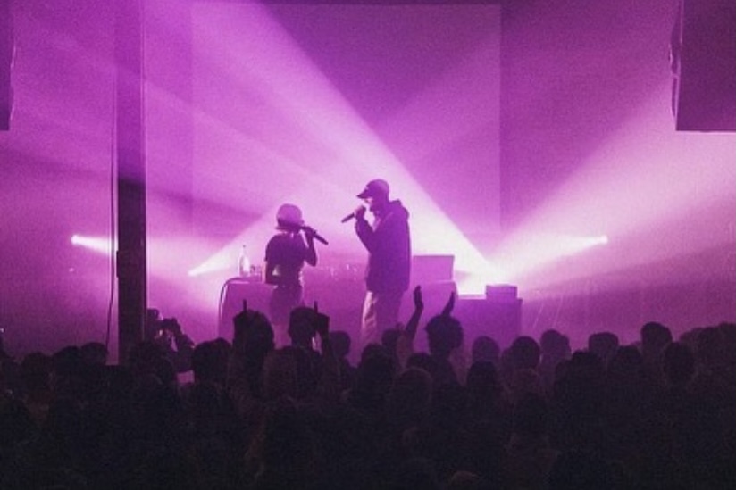 two singers silhouetted on a purple lit stage in front of a crowd