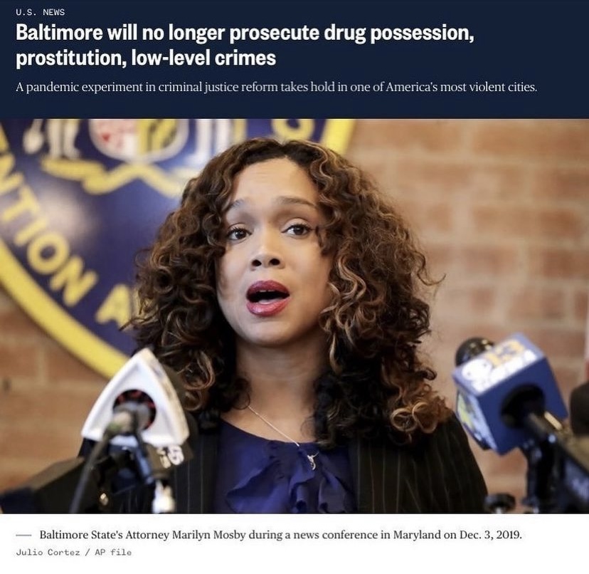a woman with curly hair stands in front of microphones with a headline above that reads "Baltimore will no longer prosecute drug possession, prostitution, low-level crimes"