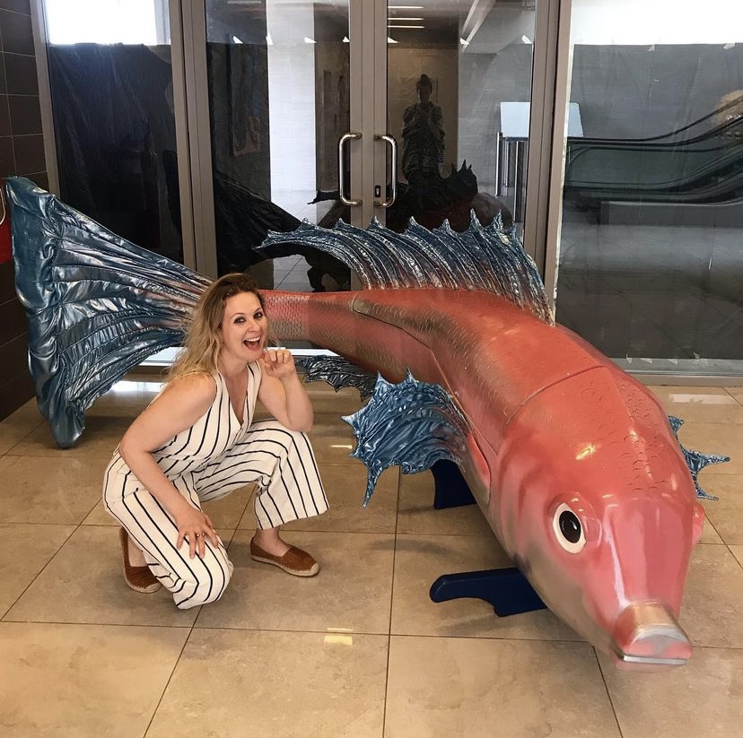 Woman kneeling next to a giant fish sculpture