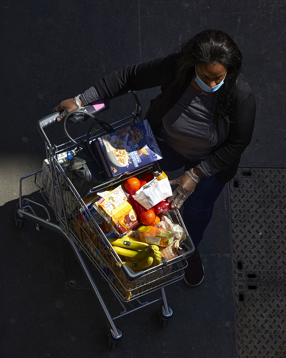view from above of a woman in a surgical mask with a grocery cart full of groceries