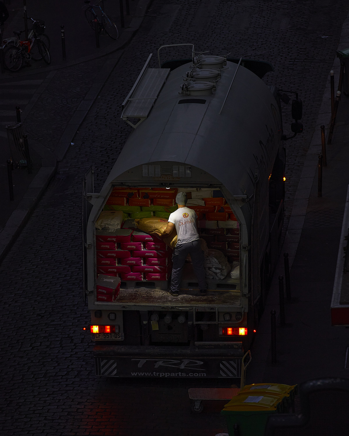 view from a distance of a man inside a truck lifting a yellow sack from a large pile