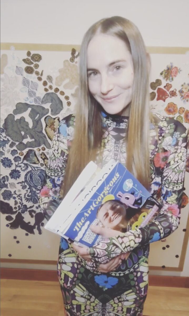 artist Gretchen Andrews in a loud spandex outfit holding a magazine and looking into the camera