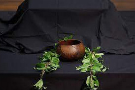 an empty wooden bowl with leaves around it sits on a black cloth surface